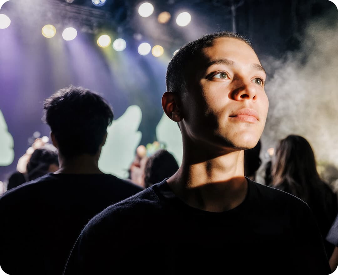 A young man illuminated by stage lighting looking up thoughtfully at a concert, with a crowd and haze in the background, for the Shubert Ticketing case study.