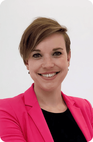 A smiling Caroline Henno, wearing a bright pink blazer and a black top, against a plain white background.