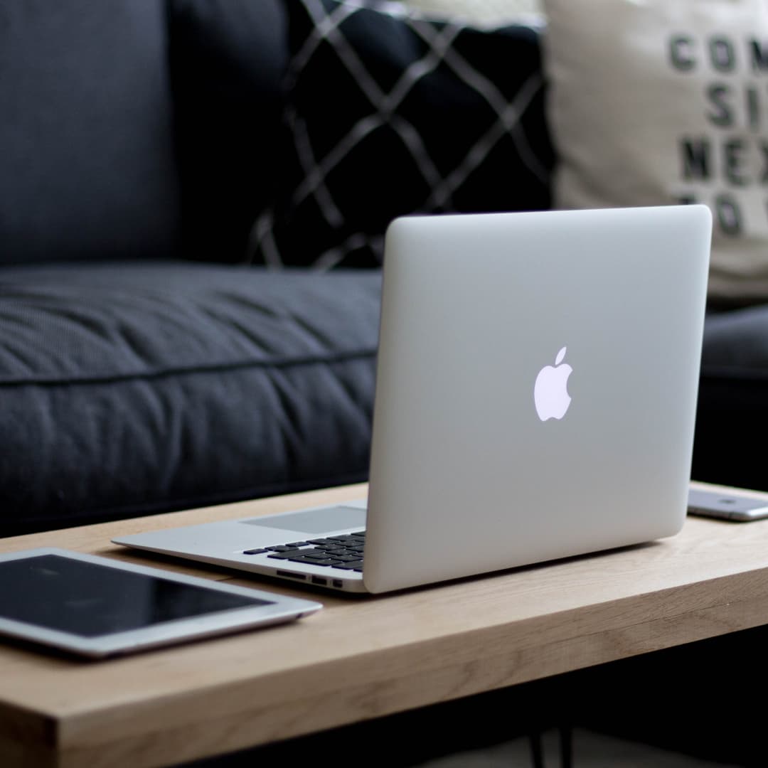 Apple iPad, Macbook, and iPhone on a coffee table with a couch in the background.