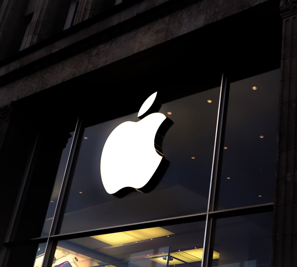 Lit up Apple logo on a glass window in a storefront.